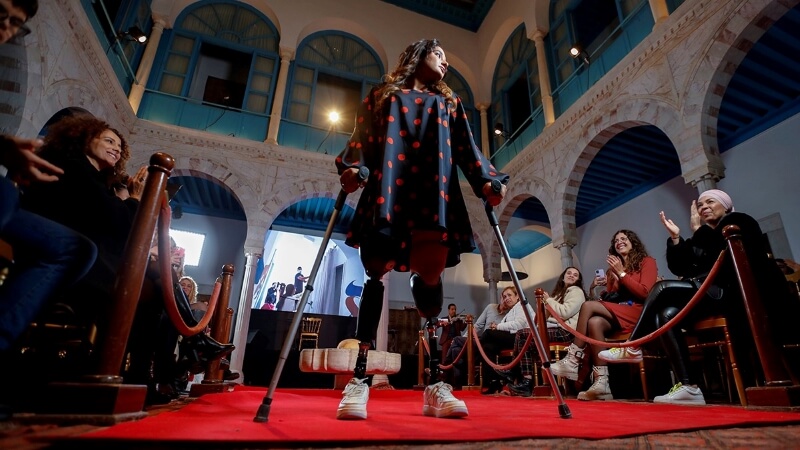 Женщина с протезами ног ходит на костылях во время показа мод, направленного на борьбу с неправильными представлениями о стандартах красоты