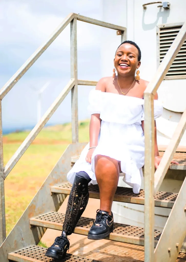 Элизабет Мангени, сидящей на лестнице и улыбающейся. На ней белое платье и золотые серьги.